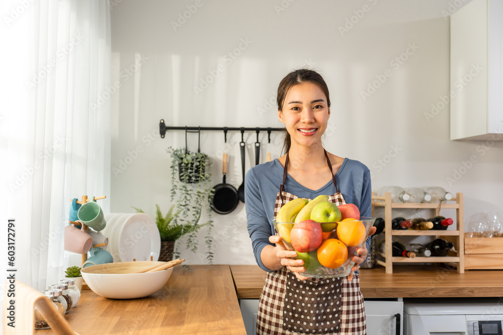 Portrait of Asian young woman hold a bowl of fruits and look at camera. 