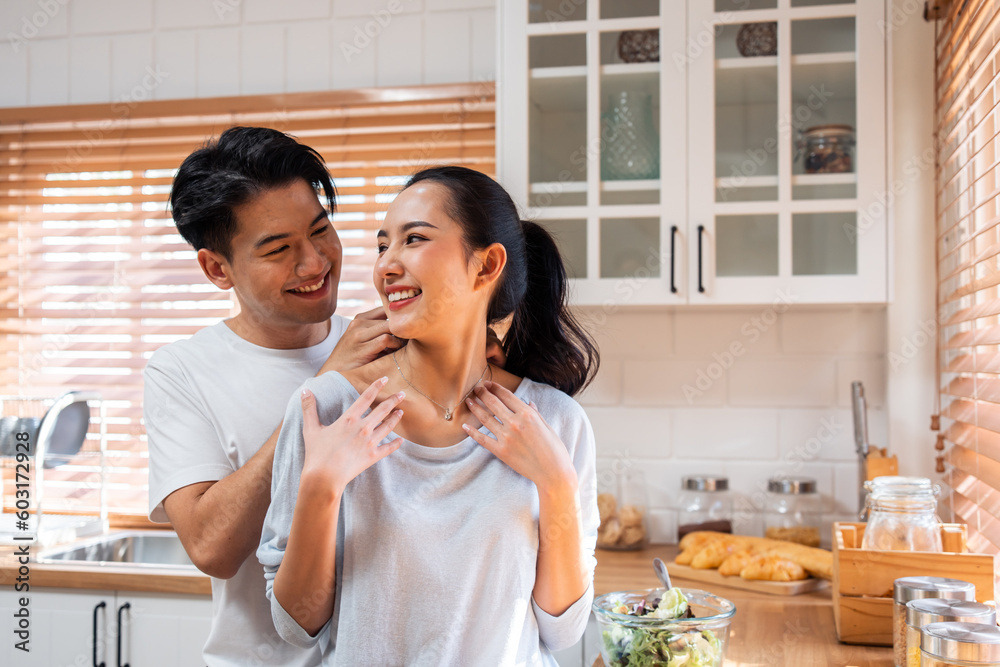 Asian romantic man making surprise girlfriend with necklace in kitchen. 