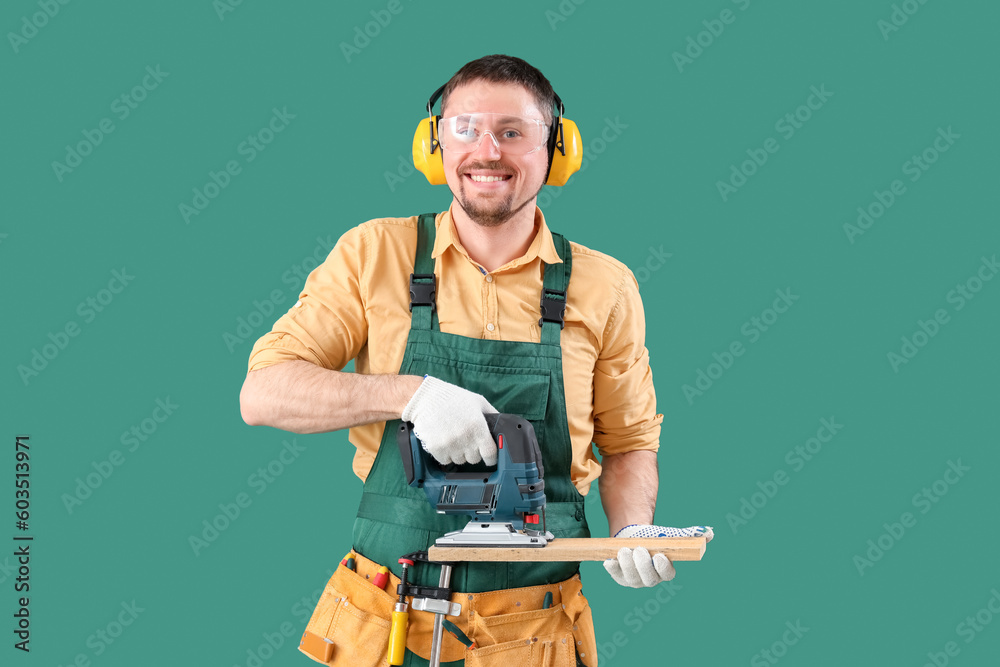 Male carpenter sawing wooden plank with jigsaw on green background