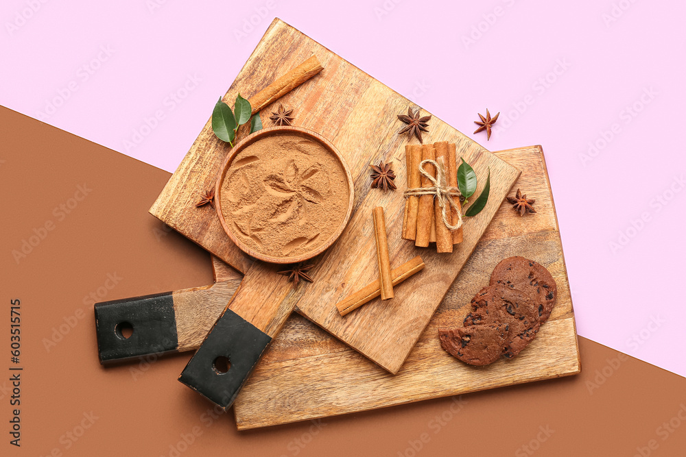 Wooden boards with bowl of cinnamon powder, sticks, anise stars and cookies on color background