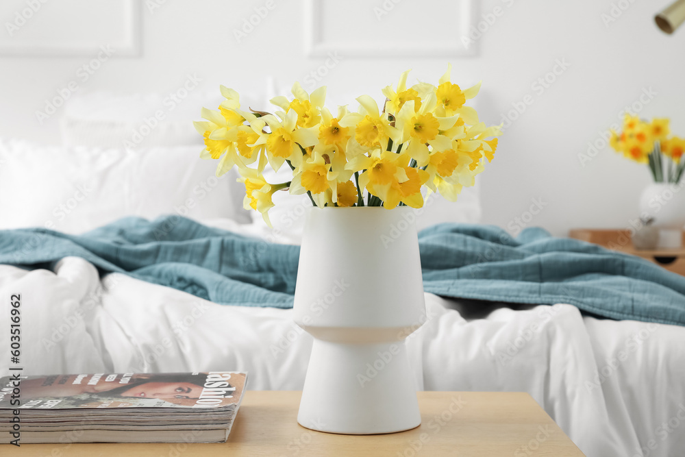 Vase with blooming narcissus flowers and magazines on bedside table