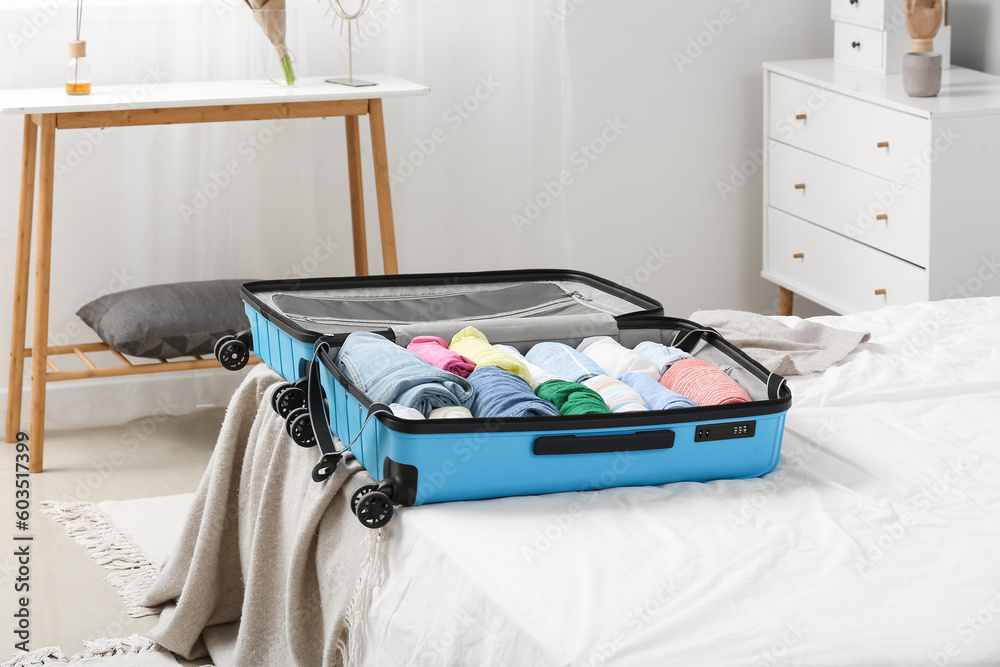 Open suitcase with folded clothes on bed in room