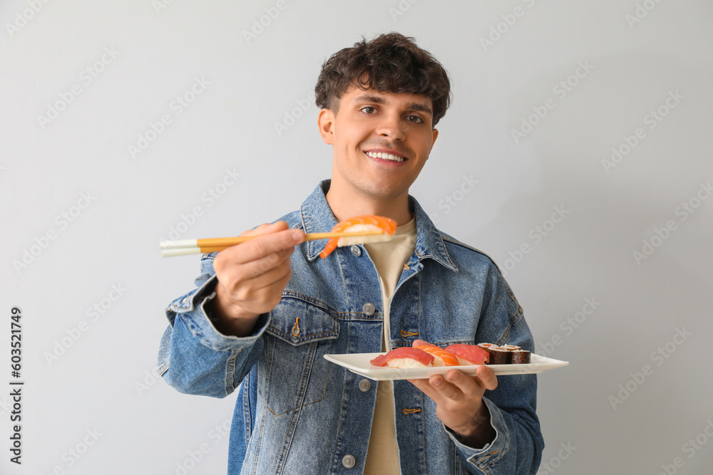 Young man with sushi on light background