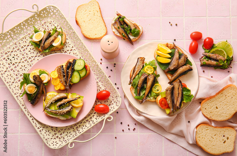 Plates of tasty sandwiches with canned smoked sprats on pink tile background