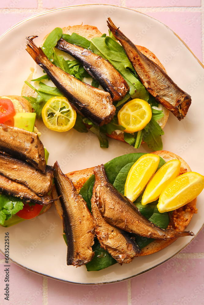 Plate of tasty sandwiches with canned smoked sprats on pink tile background