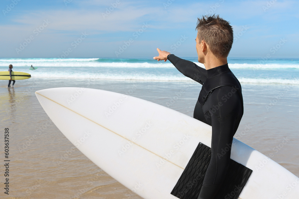 Surfer men in swimsuit holding white surfboard and pointing on the ocean waves on background. Water 