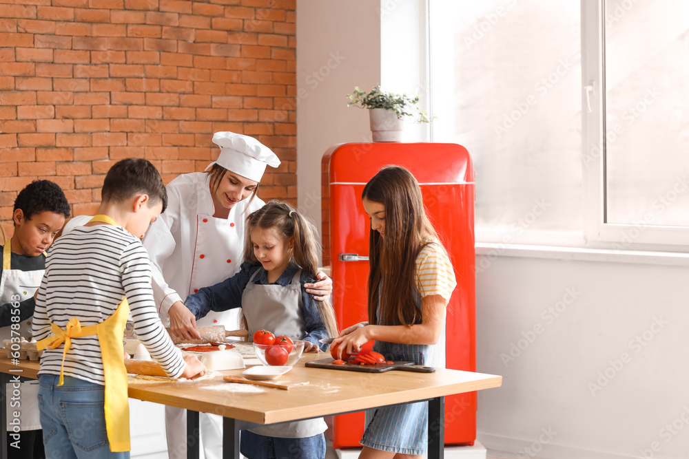 Female chef with group of little children preparing pizza during cooking class in kitchen