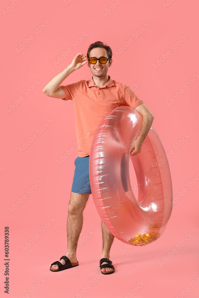 Young man with inflatable ring on pink background