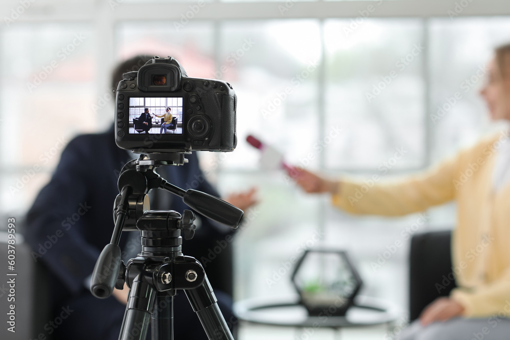 Female journalist with microphone having an interview with man on camera screen in office, closeup