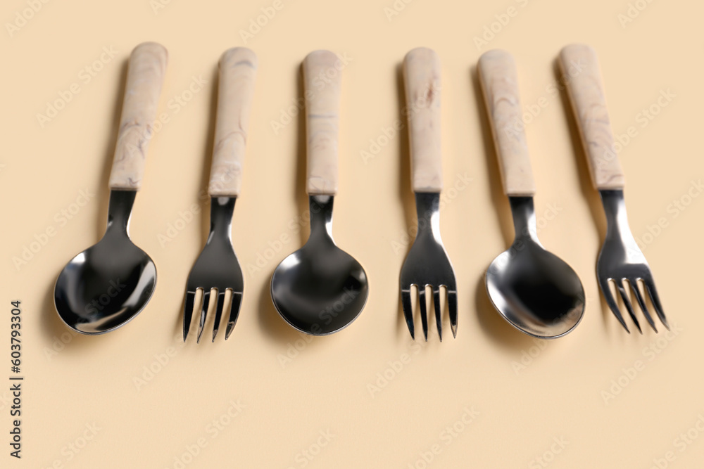 Stainless steel forks and spoons with plastic handles on beige background