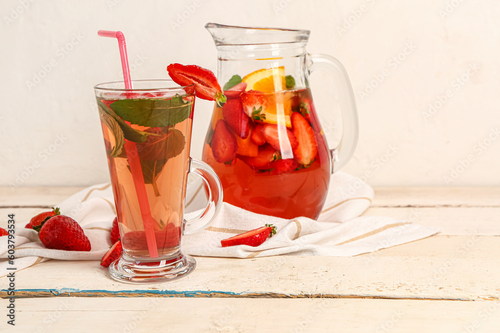 Glass and jug of tasty strawberry juice on white wooden table