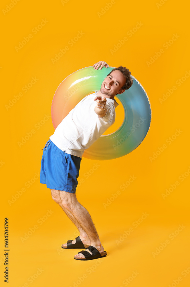 Young man with inflatable ring pointing at viewer on yellow background