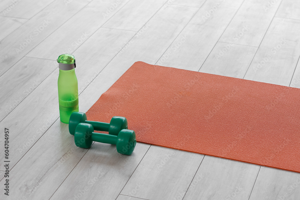 Bottle of water with dumbbells and yoga mat in gym