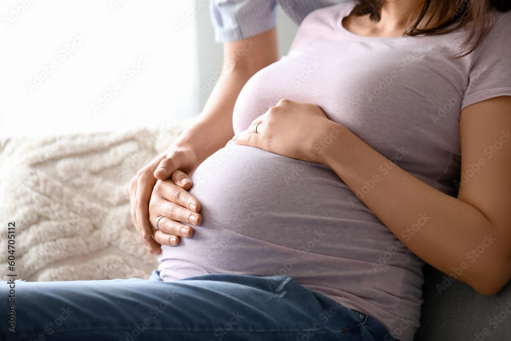 Young pregnant woman with her husband sitting on sofa at home, closeup