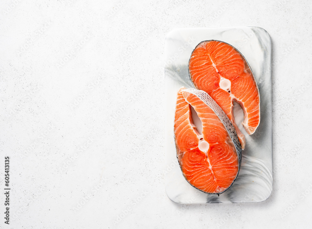 Fresh raw salmon steaks on marble board. Top view of fish on white background with copy space.