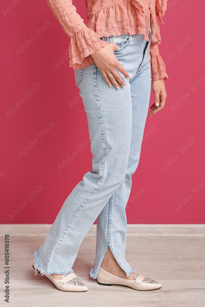 Young woman in stylish jeans near red wall