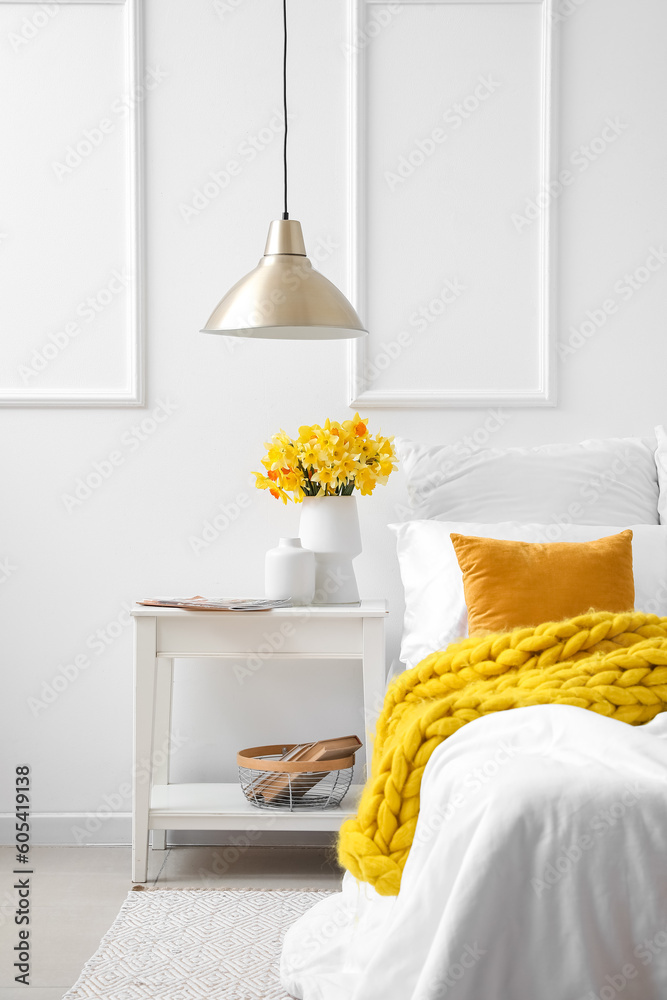 Vase with beautiful narcissus flowers on bedside table in interior of bedroom