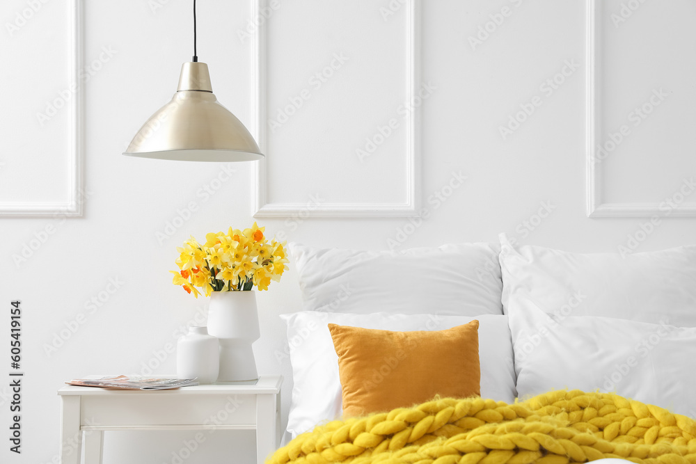 Vase with beautiful narcissus flowers on bedside table in interior of bedroom