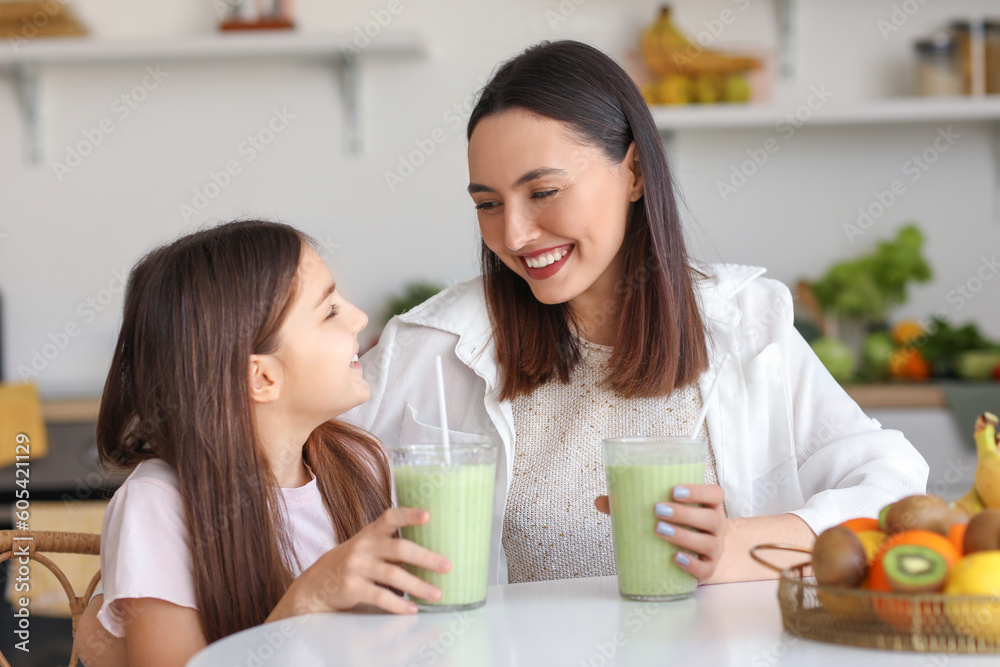 Little girl with her mother drinking green smoothie at table in kitchen