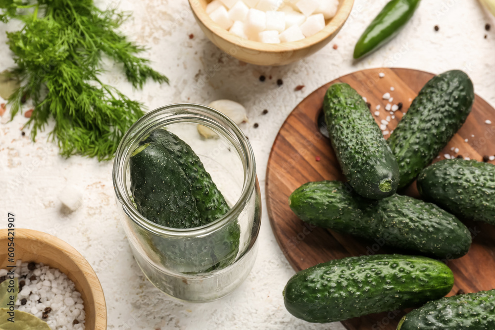 Jar and wooden board with fresh cucumbers for preservation on light background