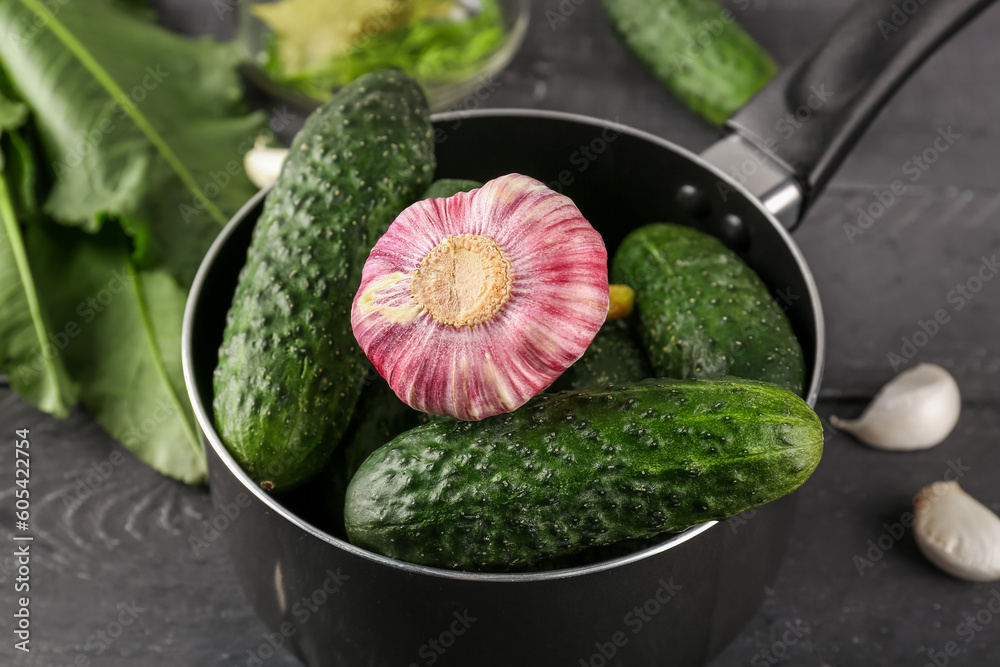 Saucepan with fresh cucumbers and garlic for preservation on dark wooden background