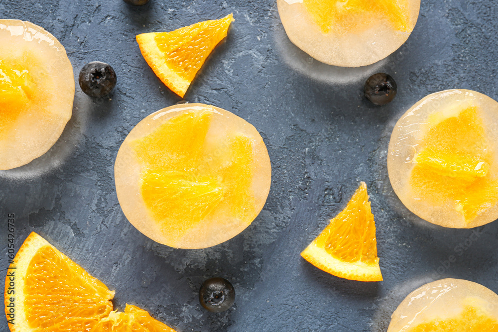 Fresh blueberry, orange and pieces frozen in ice on blue background