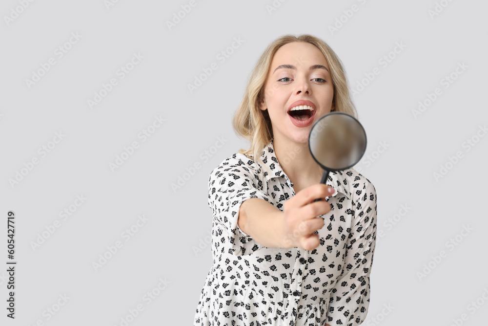 Young woman with magnifier on light background