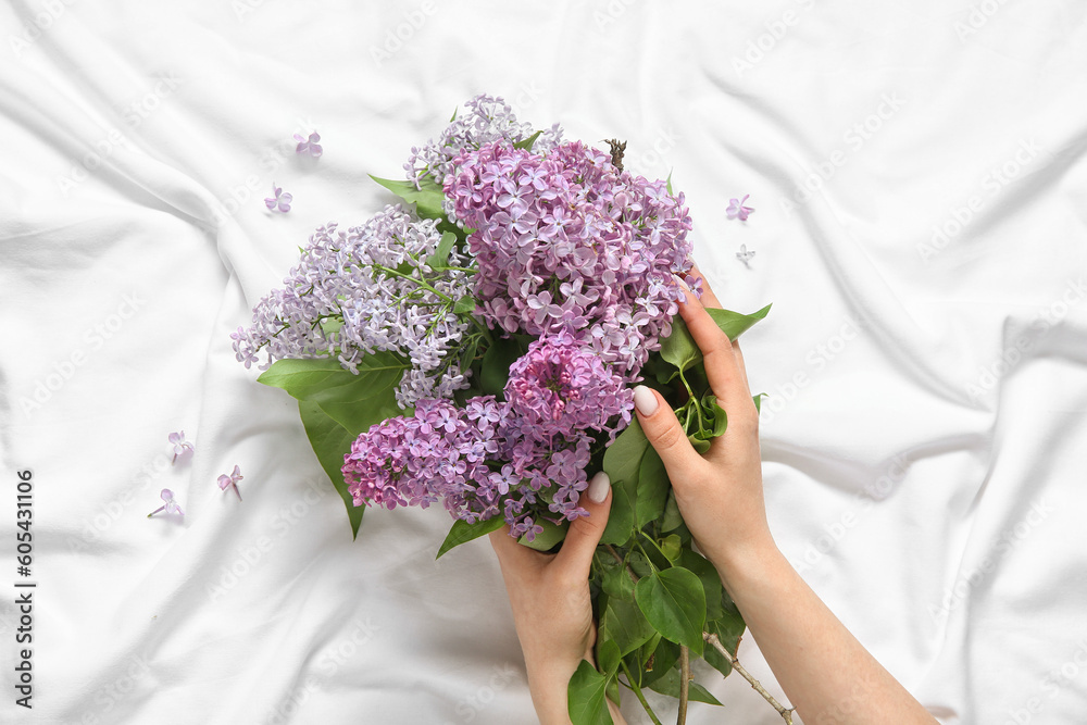 Female hands with bouquet of blooming beautiful lilac flowers on bed