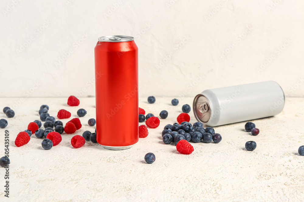 Cans of fresh soda and berries on light background