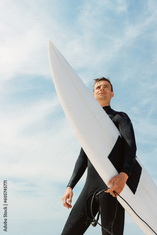 Surfer man in wetsuit holding surfboard and looking at waves