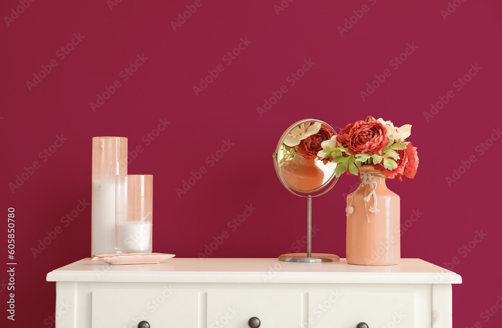 Vase with flowers, mirror and candles on table near pink wall