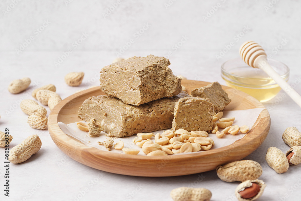 Wooden plate with pieces of tasty halva and peanuts on white background