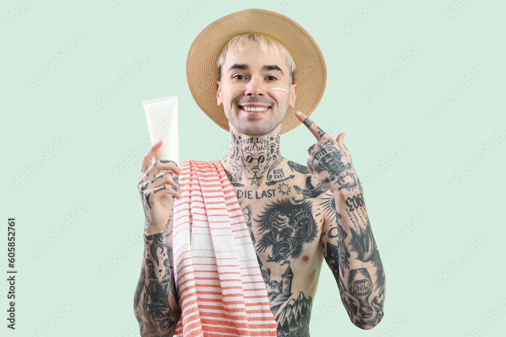 Tattooed man with sunscreen cream on light green background