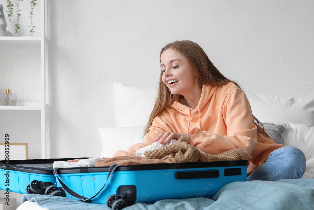 Young woman unpacking her clothes from suitcase in bedroom