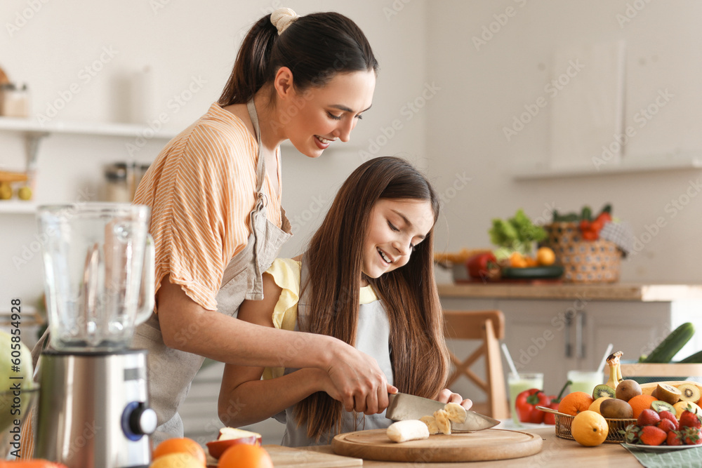 Little girl with her mother cutting banana for smoothie in kitchen