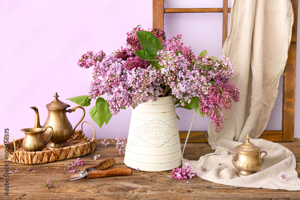 Composition with bouquet of lilacs in vase and kitchen utensils on wooden table near wall