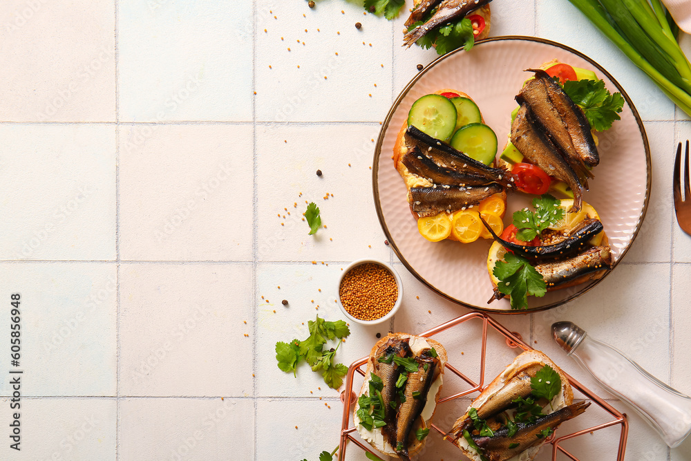 Plate and grid of tasty sandwiches with canned smoked sprats on white tile background