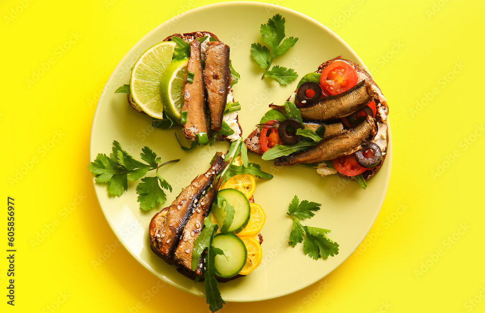 Plate of tasty sandwiches with canned smoked sprats on yellow background