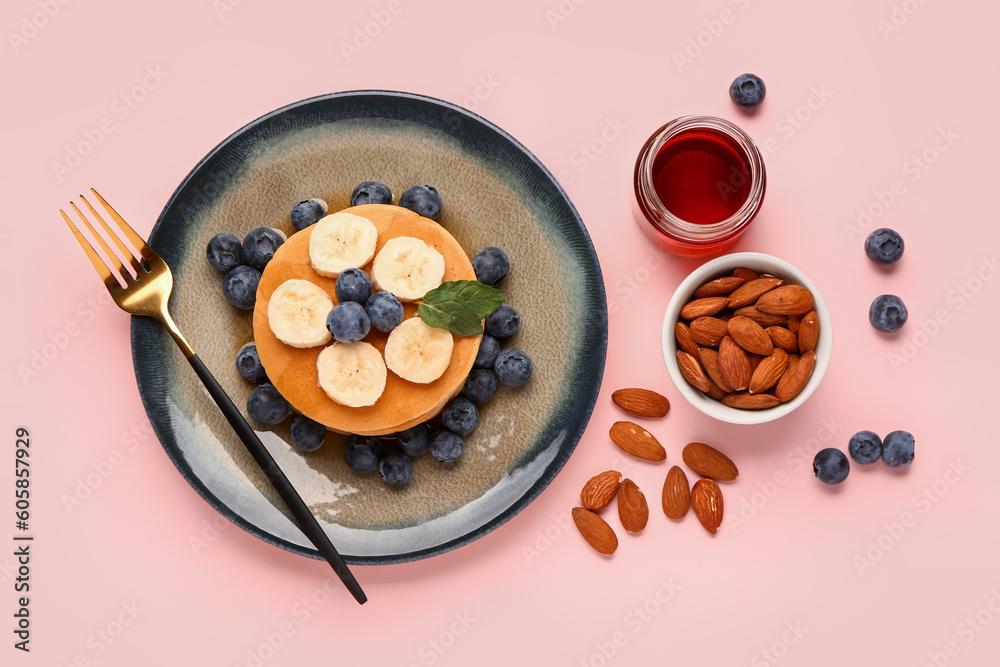 Plate with sweet pancakes, nuts and honey on pink background