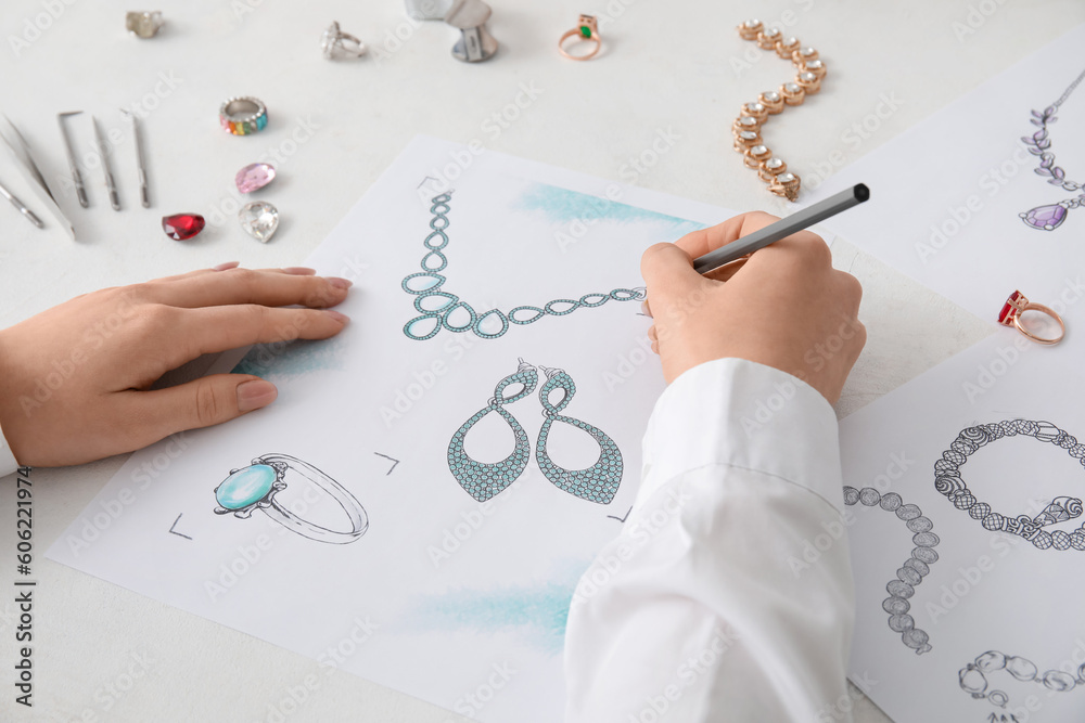 Female jeweler drawing adornment on white table, closeup