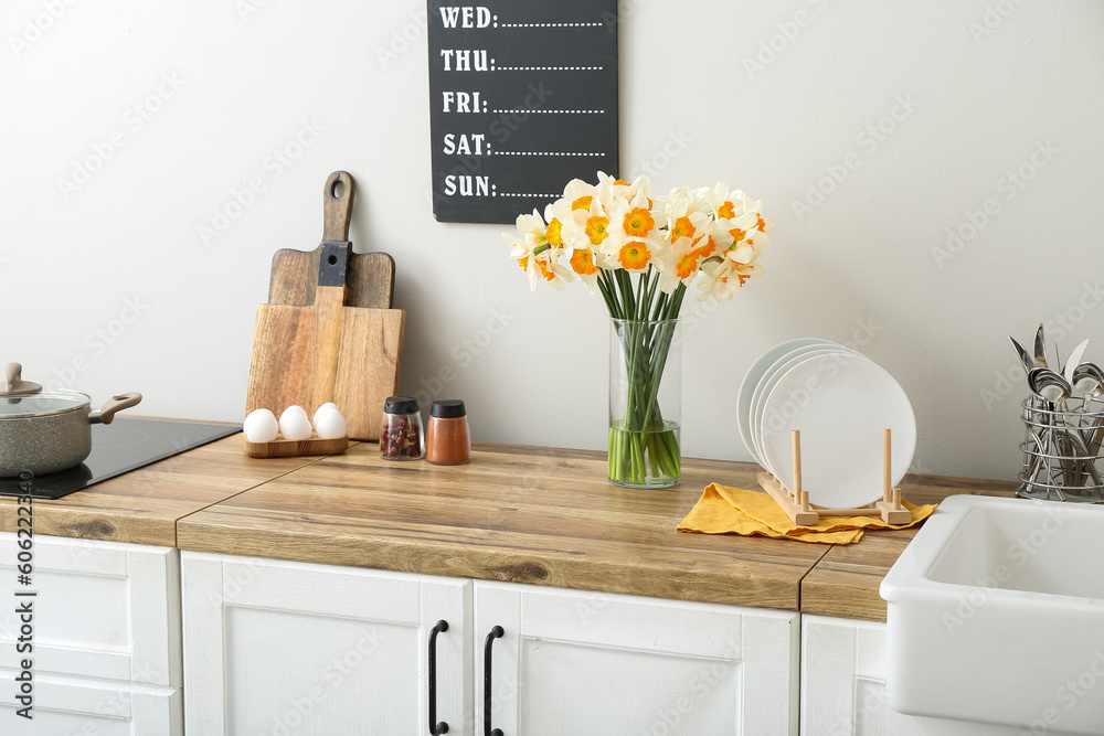 Vase with blooming narcissus flowers on wooden counter in interior of modern kitchen