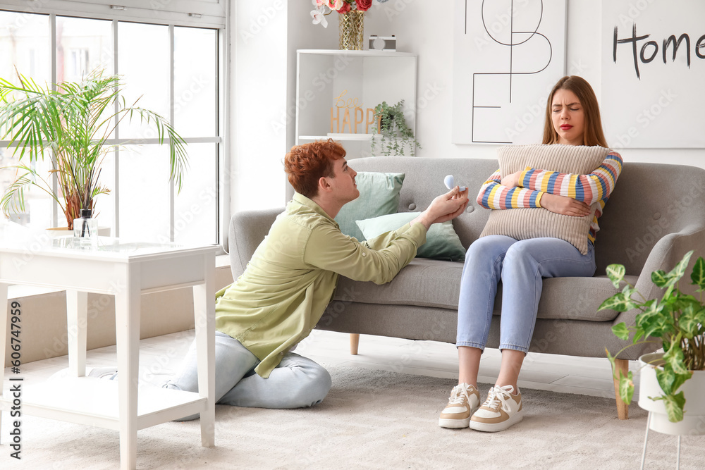 Young man proposing to his thoughtful girlfriend at home