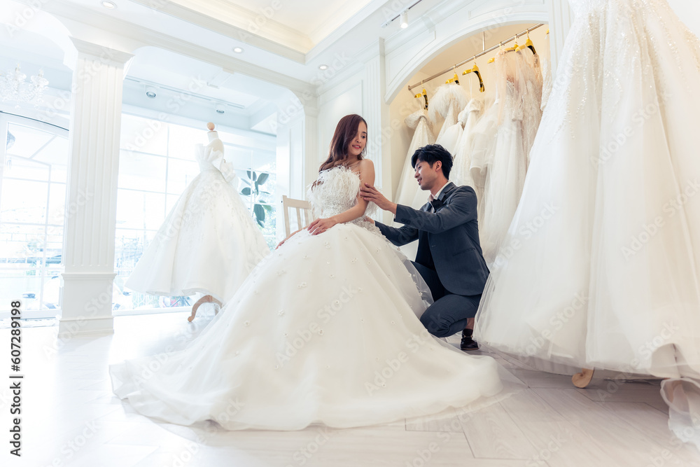 Asian beautiful bride trying on wedding gown with her fiance in studio. 