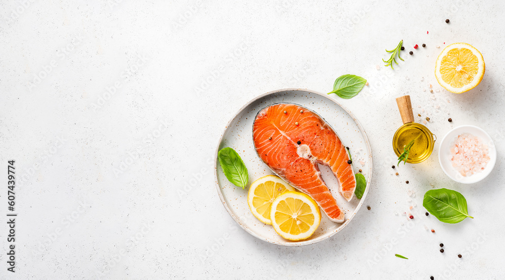 Fresh raw salmon steaks with spices, lemons and pink salt on white plate. Top view of fish with copy