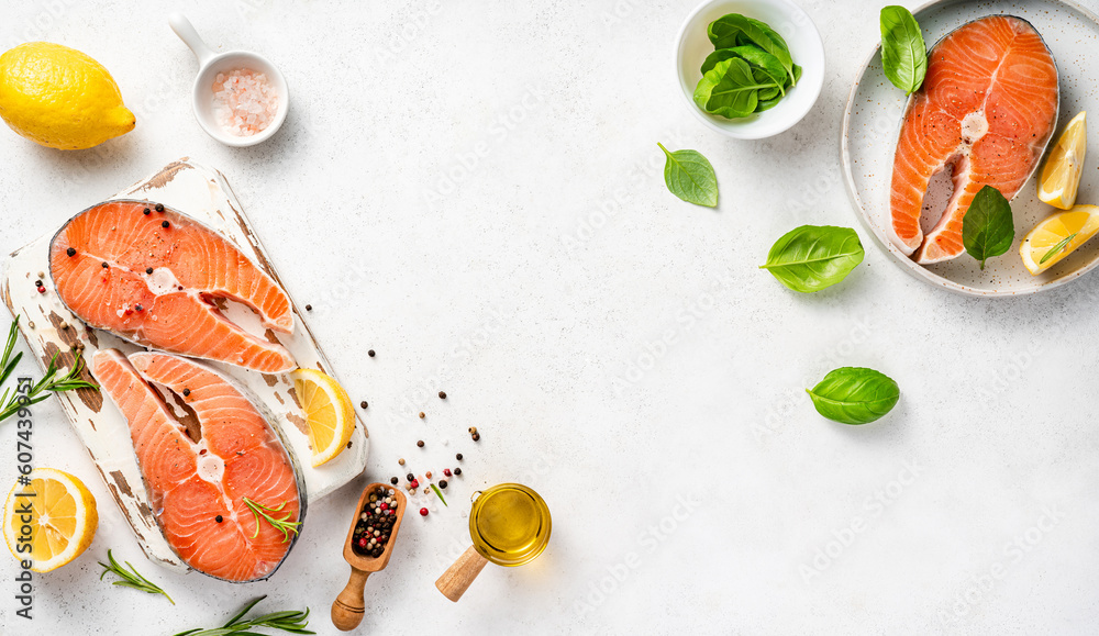 Fresh raw salmon steaks with spices and lemons on wooden board. Top view of fish and olive oil on wh