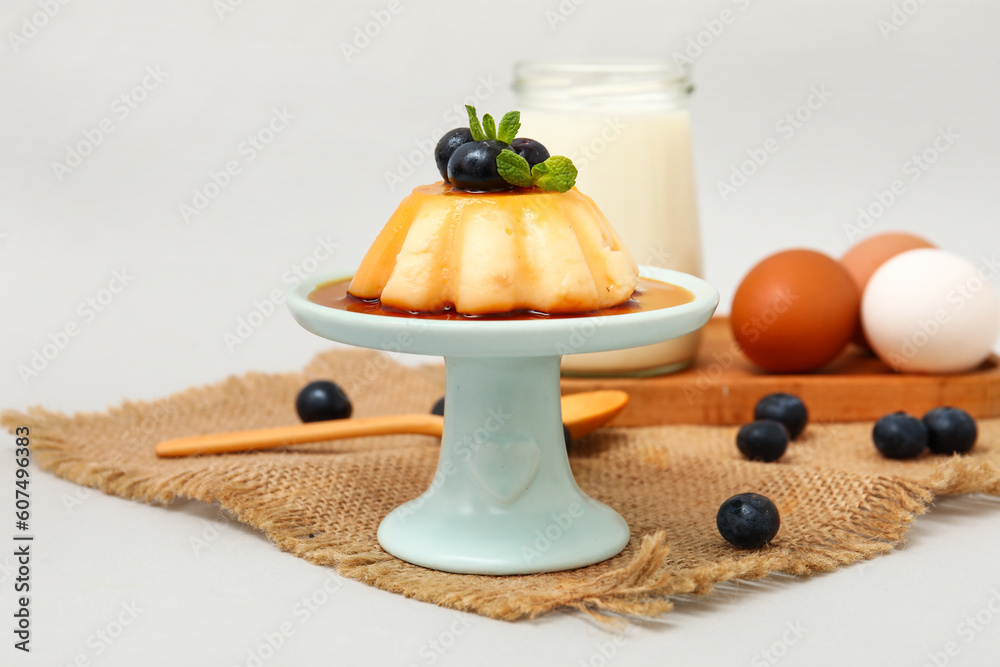 Dessert stand with delicious pudding and blueberries covered by caramel syrup on grey background