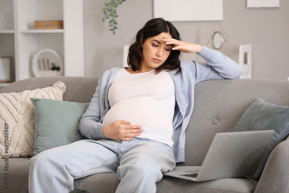 Tired young pregnant woman working with laptop at home