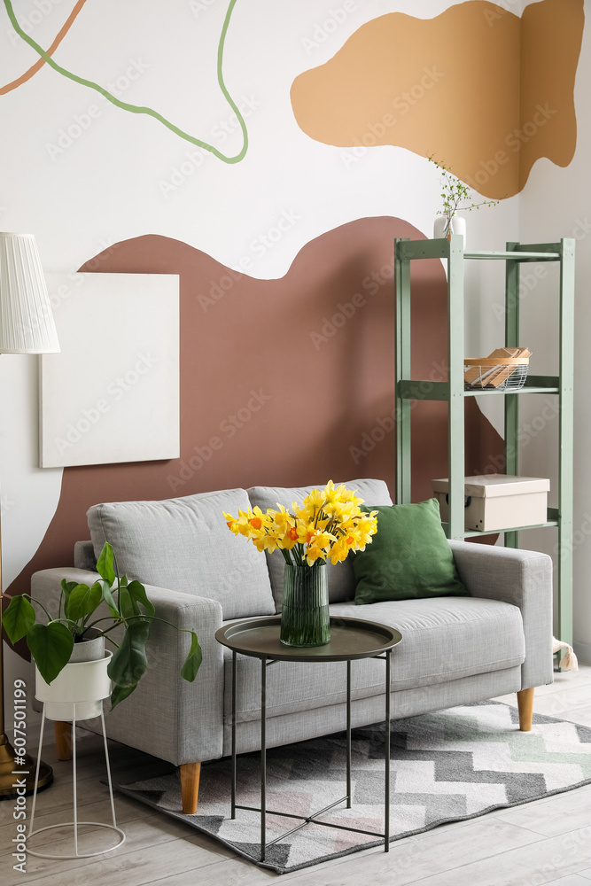 Interior of stylish living room with cozy grey sofa and blooming narcissus flowers on coffee table