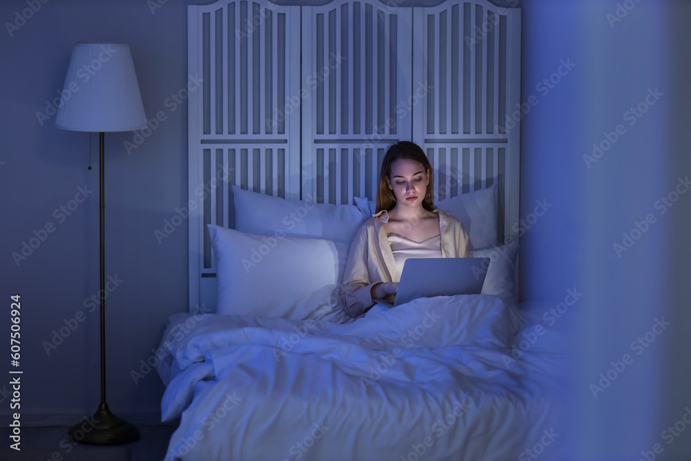 Young woman using laptop in bedroom at night