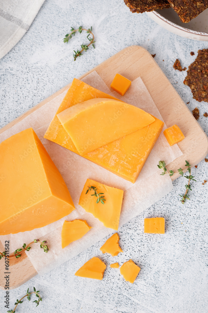 Board with tasty cheddar cheese and thyme on light background